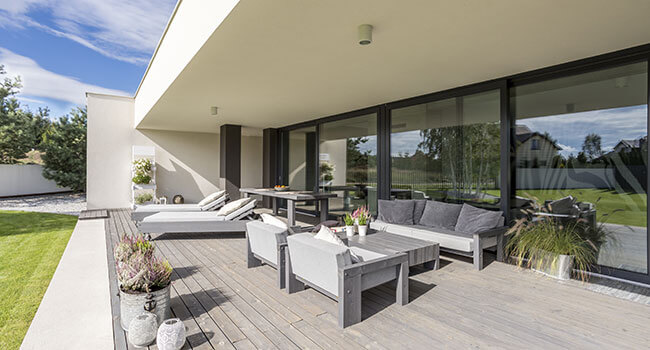 Holzterrasse mit großer Fensterfront, Sitzsofa und zwei Sessel, Tisch, Holzliegen